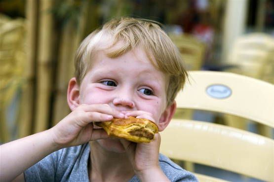 Jongen, die een saucijzenbroodje eet